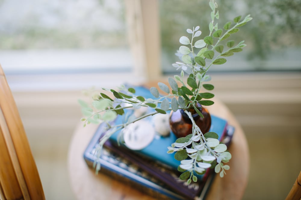 A quiet side table with eucalyptus, a teal notebook, and a book, the feel of handling a few minutes of paperwork at home.