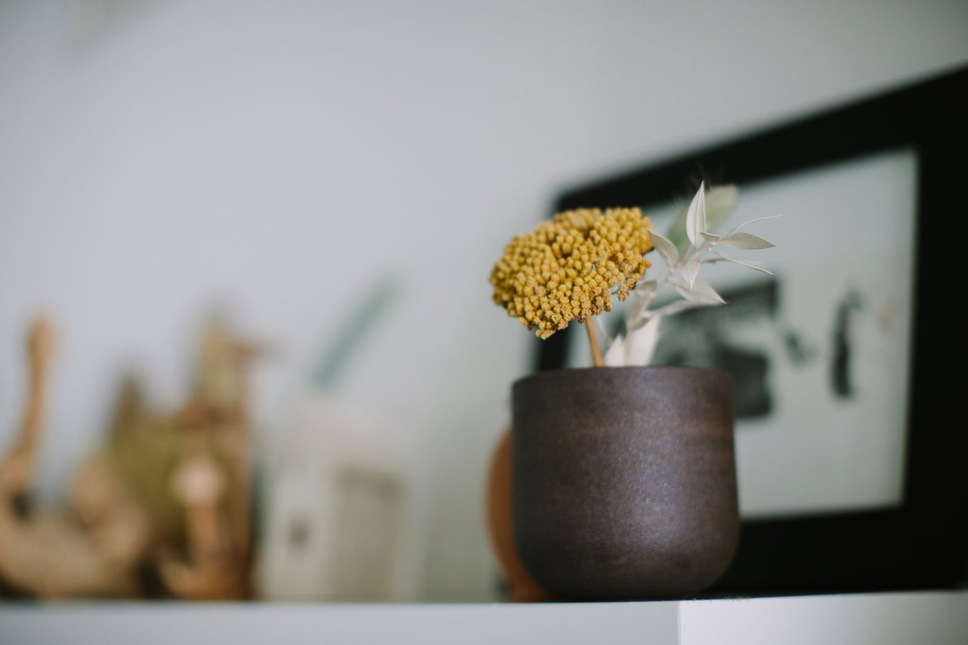 A dried yellow flower in a small brown vase on a shelf, a quiet moment of detail.
