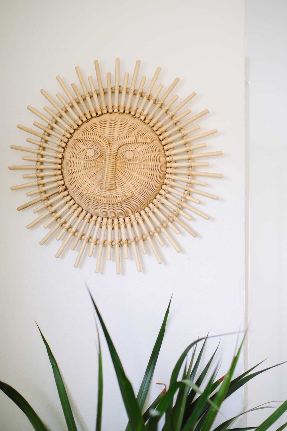 A rattan sun face wall hanging above a green plant